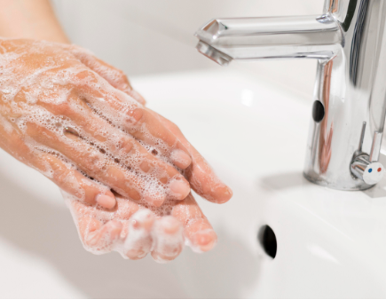 Hands lathered with soap near a sink faucet.